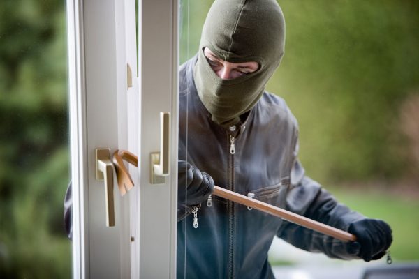 Einbrecher mit Brecheisen beim Versuch durch ein Fenster einzubrechen